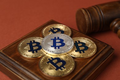 Photo of Cryptocurrency. Bitcoins and judge's gavel on red-brown background, closeup