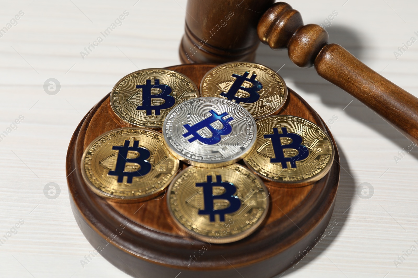 Photo of Cryptocurrency. Bitcoins and judge's gavel on white wooden table, closeup