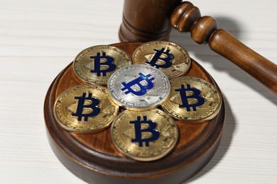 Photo of Cryptocurrency. Bitcoins and judge's gavel on white wooden table, closeup