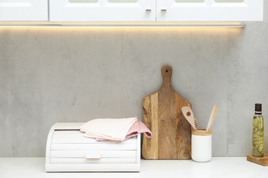 Photo of Clean waffle towels, utensils, breadbox and cutting board on countertop in kitchen
