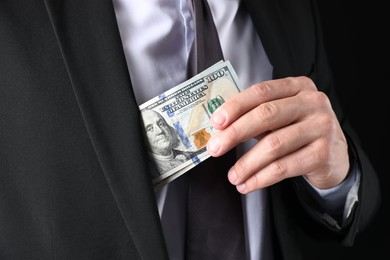 Photo of Man putting dollars in pocket on black background, closeup