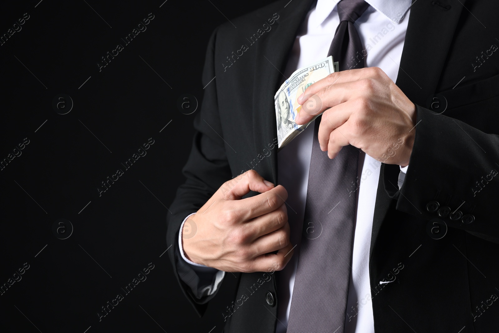 Man putting dollars in pocket on black background, closeup. Space for text Photo of Man putting dollars in pocket on black background, closeup. Space for text
