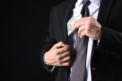 Photo of Man putting dollars in pocket on black background, closeup. Space for text
