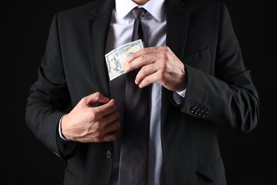 Photo of Man putting dollars in pocket on black background, closeup