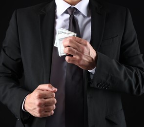 Photo of Man putting dollars in pocket on black background, closeup