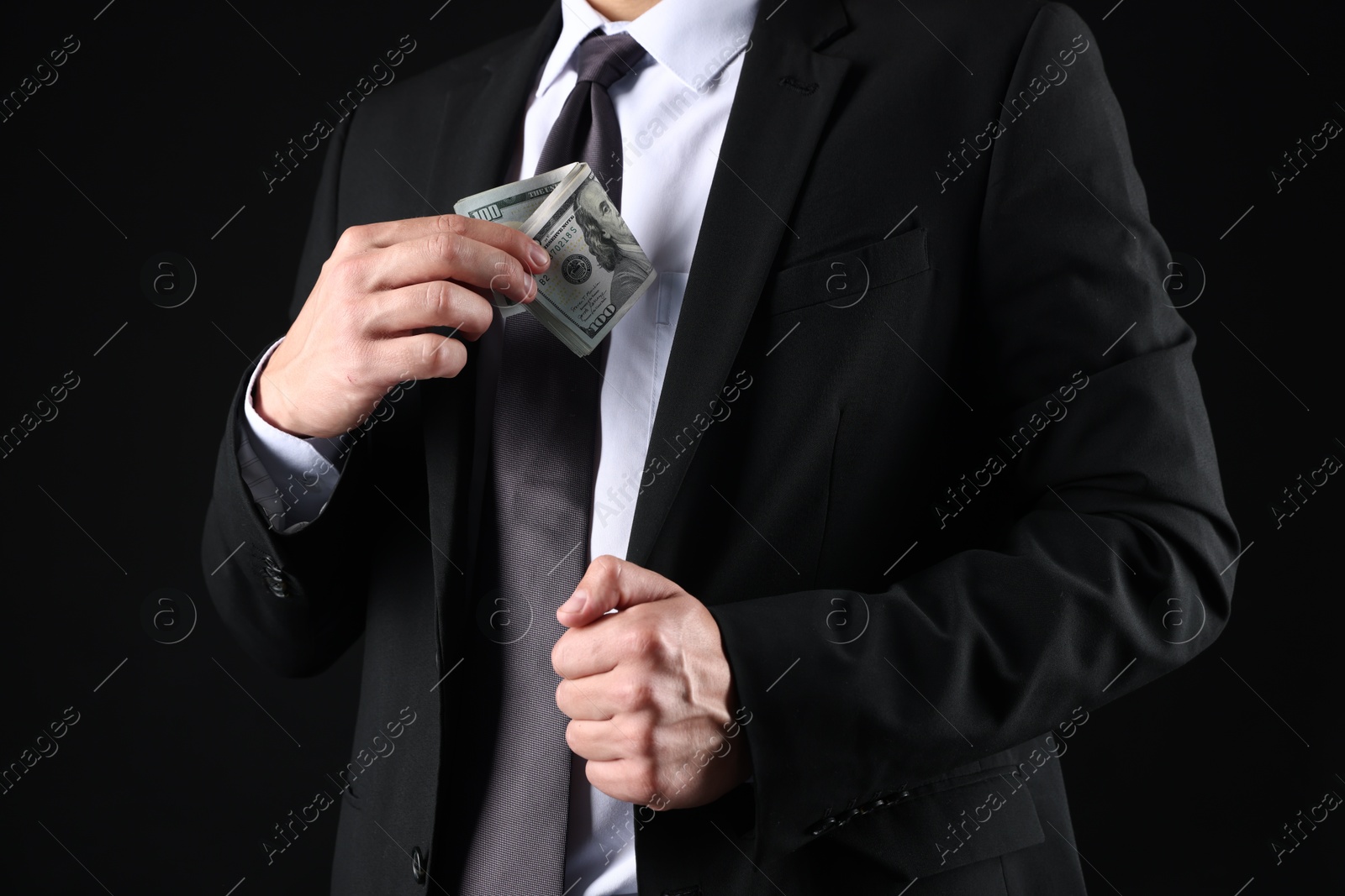 Man putting dollars in pocket on black background, closeup Photo of Man putting dollars in pocket on black background, closeup