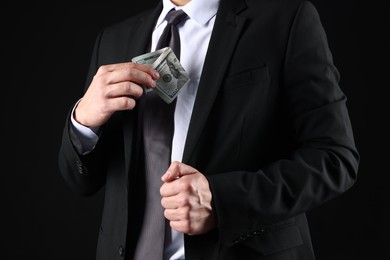 Photo of Man putting dollars in pocket on black background, closeup