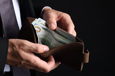 Photo of Man holding wallet with dollars on black background, closeup