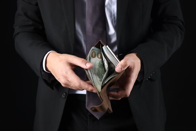 Photo of Man holding wallet with dollars on black background, closeup