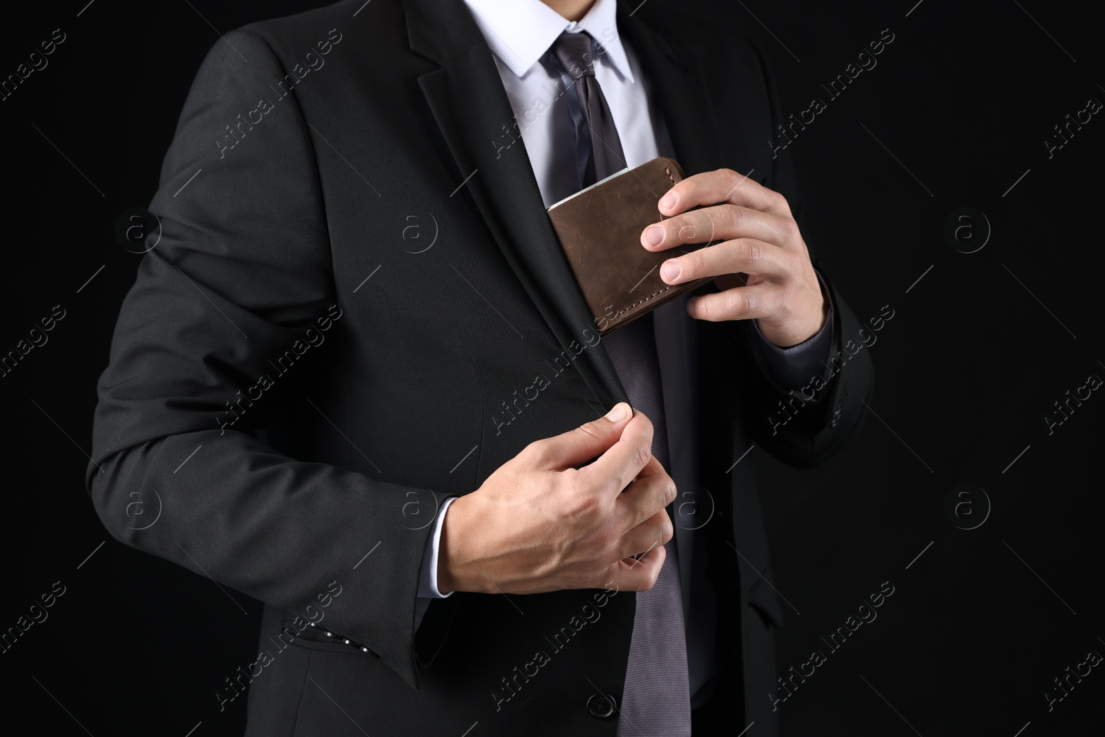 Man putting wallet with dollars into his pocket on black background, closeup Photo of Man putting wallet with dollars into his pocket on black background, closeup