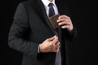 Photo of Man putting wallet with dollars into his pocket on black background, closeup