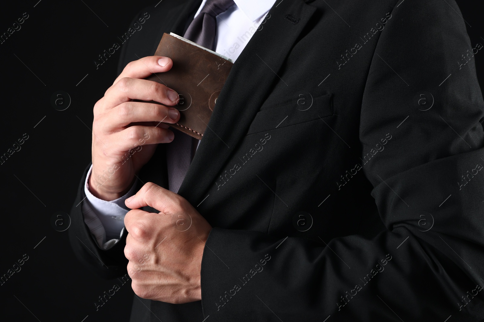 Man putting wallet with dollars into his pocket on black background, closeup Photo of Man putting wallet with dollars into his pocket on black background, closeup