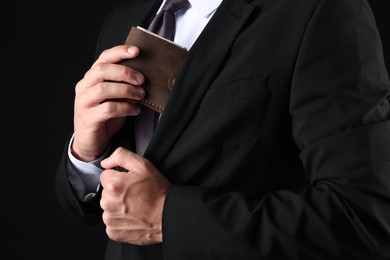 Photo of Man putting wallet with dollars into his pocket on black background, closeup