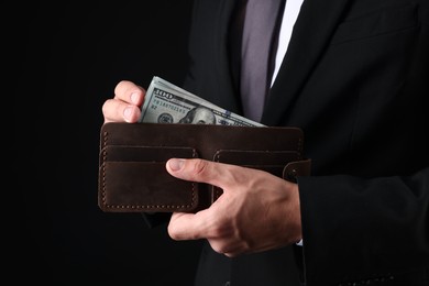Photo of Man holding wallet with dollars on black background, closeup