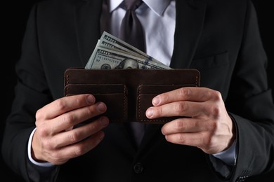 Photo of Man holding wallet with dollars on black background, closeup