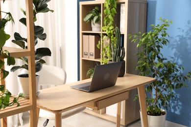 Photo of Stylish workplace with laptop on wooden desk and floral decor in office. Biophilic interior design