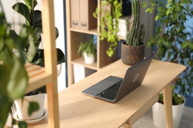 Photo of Stylish workplace with laptop on wooden desk and floral decor in office. Biophilic interior design