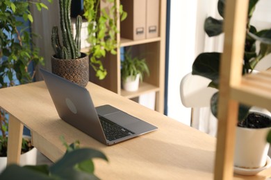 Photo of Stylish workplace with laptop on wooden desk and floral decor in office. Biophilic interior design