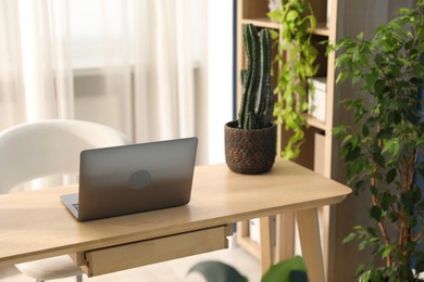 Photo of Stylish workplace with laptop on wooden desk and floral decor in office. Biophilic interior design