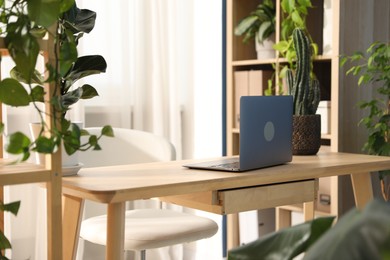 Photo of Stylish workplace with laptop on wooden desk and floral decor in office. Biophilic interior design