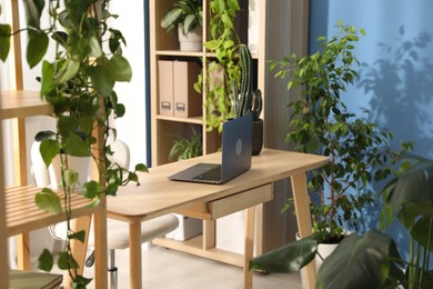 Photo of Stylish workplace with laptop on wooden desk and floral decor in office. Biophilic interior design