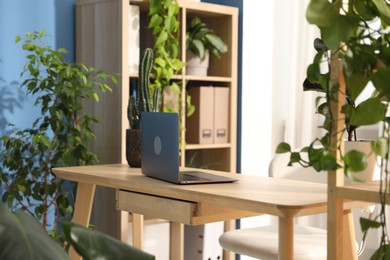 Photo of Stylish workplace with laptop on wooden desk and floral decor in office. Biophilic interior design