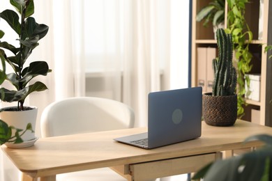 Photo of Stylish workplace with laptop on wooden desk and floral decor in office. Biophilic interior design