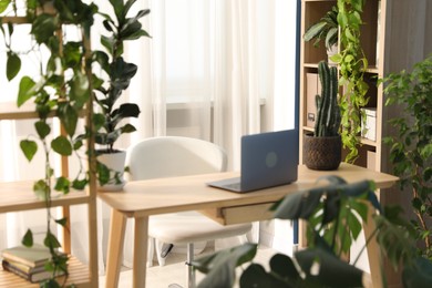 Photo of Stylish workplace with laptop on wooden desk and floral decor in office. Biophilic interior design