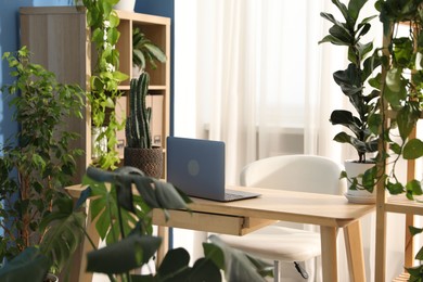 Photo of Stylish workplace with laptop on wooden desk and floral decor in office. Biophilic interior design