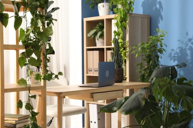 Photo of Stylish workplace with laptop on wooden desk and floral decor in office. Biophilic interior design