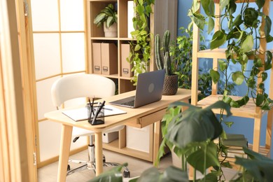 Photo of Stylish workplace with laptop, stationery and floral decor in office. Biophilic interior design