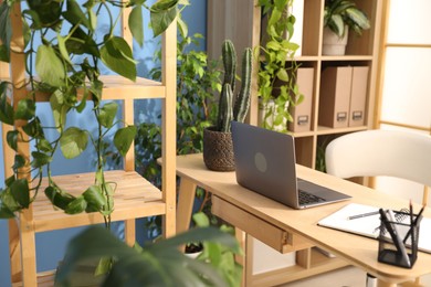 Photo of Stylish workplace with laptop, stationery and floral decor in office. Biophilic interior design