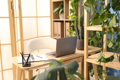 Photo of Stylish workplace with laptop, stationery and floral decor in office. Biophilic interior design