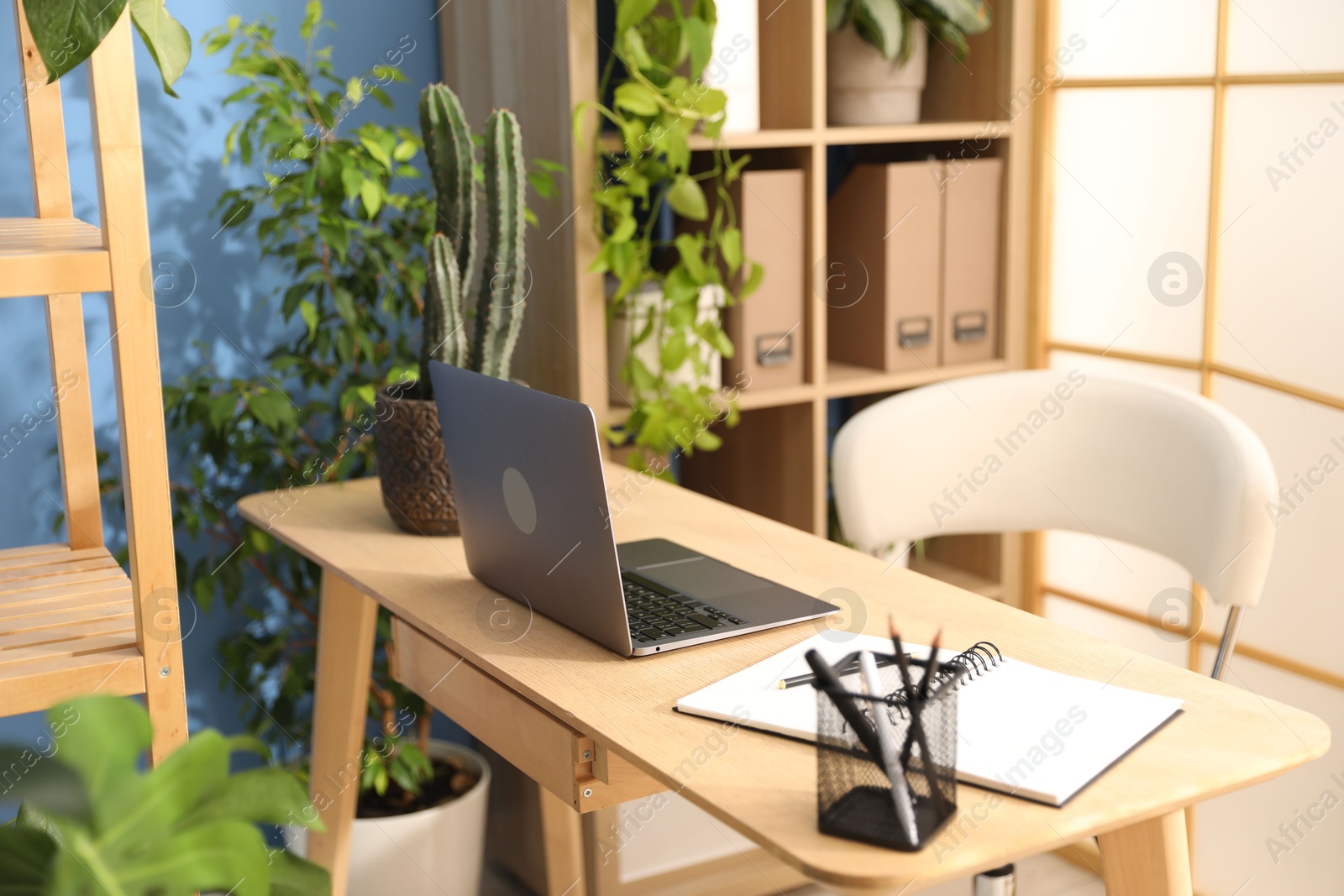 Photo of Stylish workplace with laptop, stationery and floral decor in office. Biophilic interior design