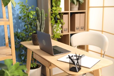 Photo of Stylish workplace with laptop, stationery and floral decor in office. Biophilic interior design