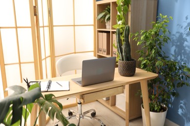 Photo of Stylish workplace with laptop, stationery and floral decor in office. Biophilic interior design
