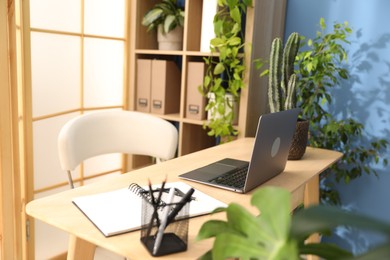 Photo of Stylish workplace with laptop, stationery and floral decor in office. Biophilic interior design