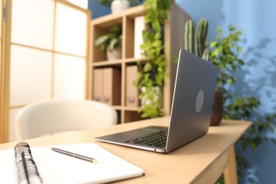 Photo of Stylish workplace with laptop, stationery and floral decor in office, closeup. Biophilic interior design