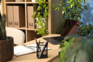 Photo of Stylish workplace with laptop, stationery and floral decor in office. Biophilic interior design