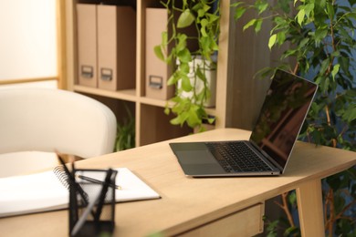 Photo of Stylish workplace with laptop, stationery and floral decor in office. Biophilic interior design