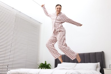Photo of Happy woman in pyjama jumping on bed at home, low angle view