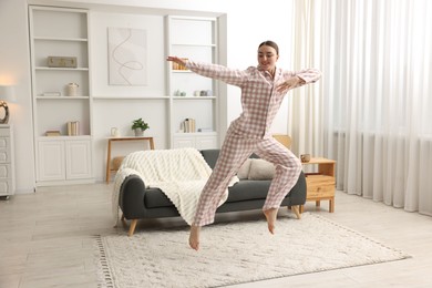Photo of Happy woman in pyjama jumping at home, space for text