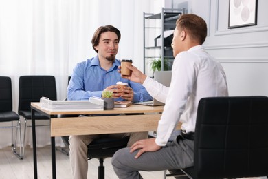 Photo of Coworkers with coffee discussing project together at desk in office
