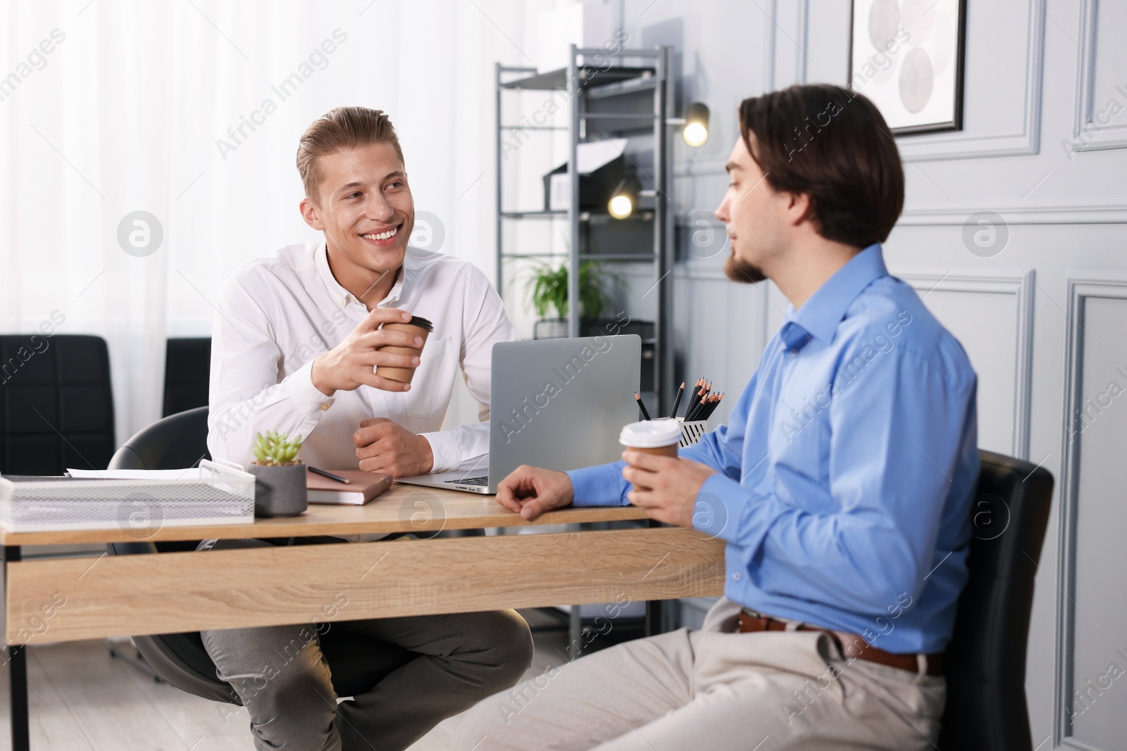 Coworkers with coffee discussing project together at desk in office Photo of Coworkers with coffee discussing project together at desk in office