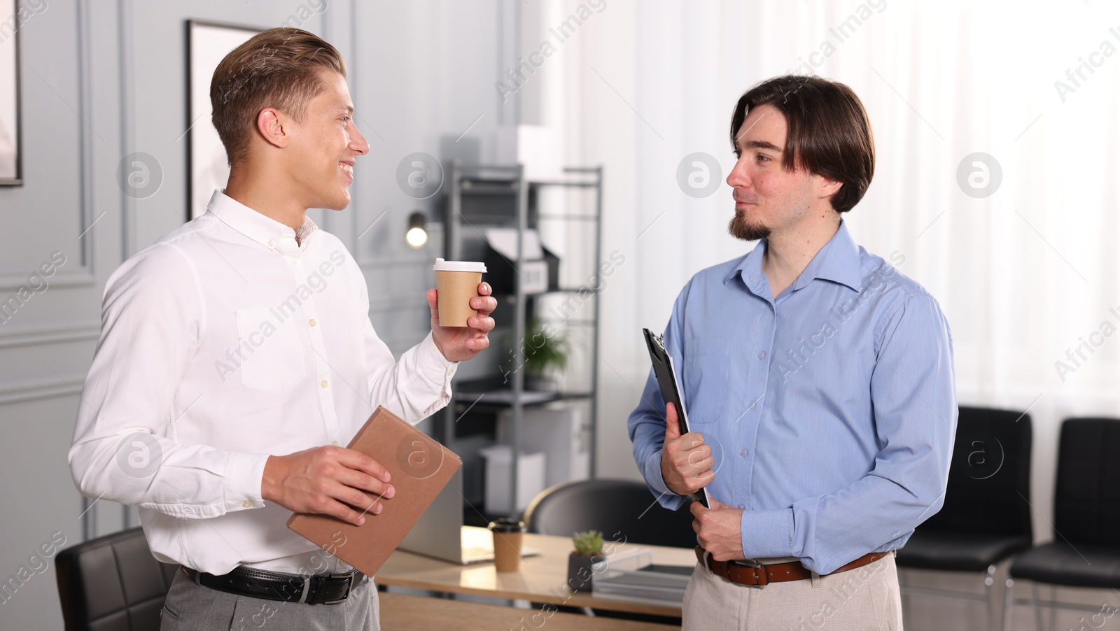 Coworkers with paperwork, coffee and tablet having conversation in office Photo of Coworkers with paperwork, coffee and tablet having conversation in office