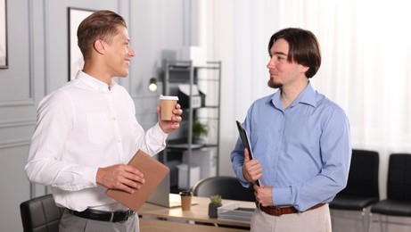 Photo of Coworkers with paperwork, coffee and tablet having conversation in office