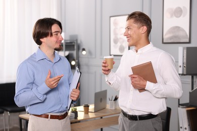 Photo of Coworkers with paperwork, coffee and tablet having conversation in office