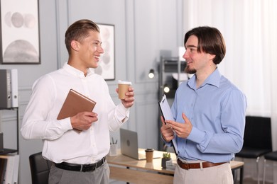 Photo of Coworkers with paperwork, coffee and tablet having conversation in office