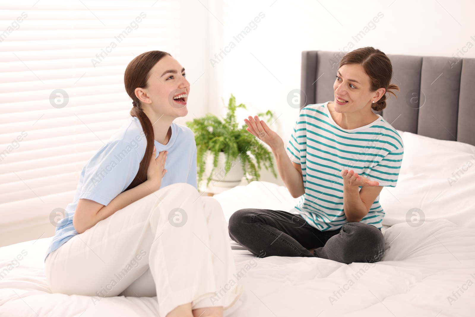 Photo of Woman talking to her friend and laughing on bed at home