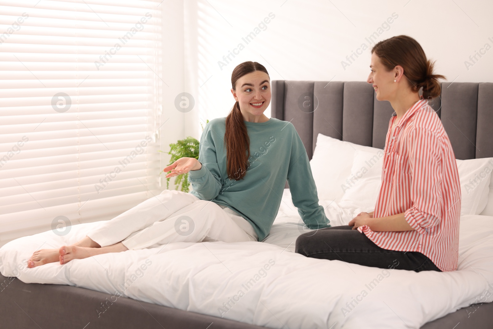 Photo of Woman talking to her friend and laughing on bed at home